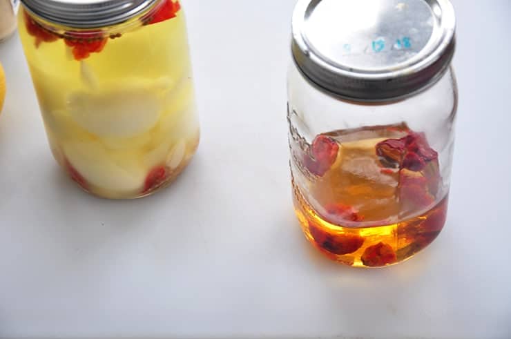 To mason jars on a white backdrop. One is filled with pickled eggs and the other the vodka.