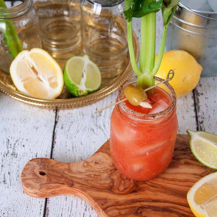 Bloody Caesar cocktail on a cutting board with various fruits and sides that go along with it