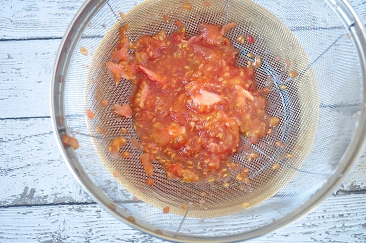 Tomato seeds and pulp straining into bowl.