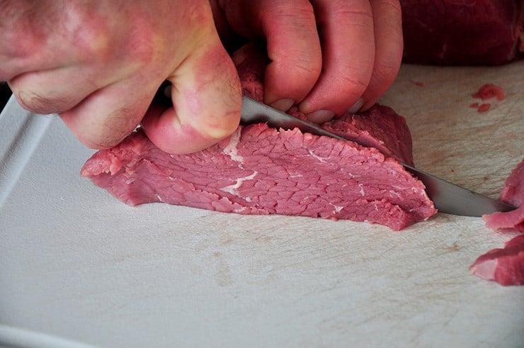 Cutting eye of round roast before marinating.