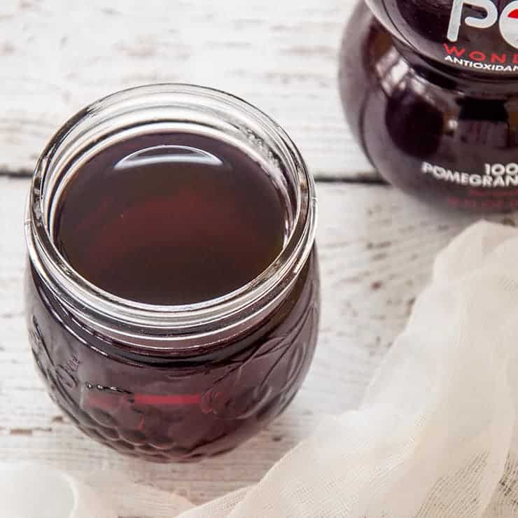 Side view of grenadine in half-pint mason jar and a bottle of Pom in the background.