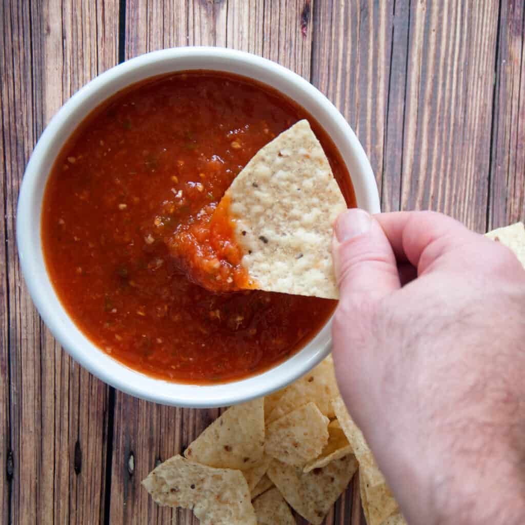 A hand dipping chips into our homemade salsa in a white bowl.