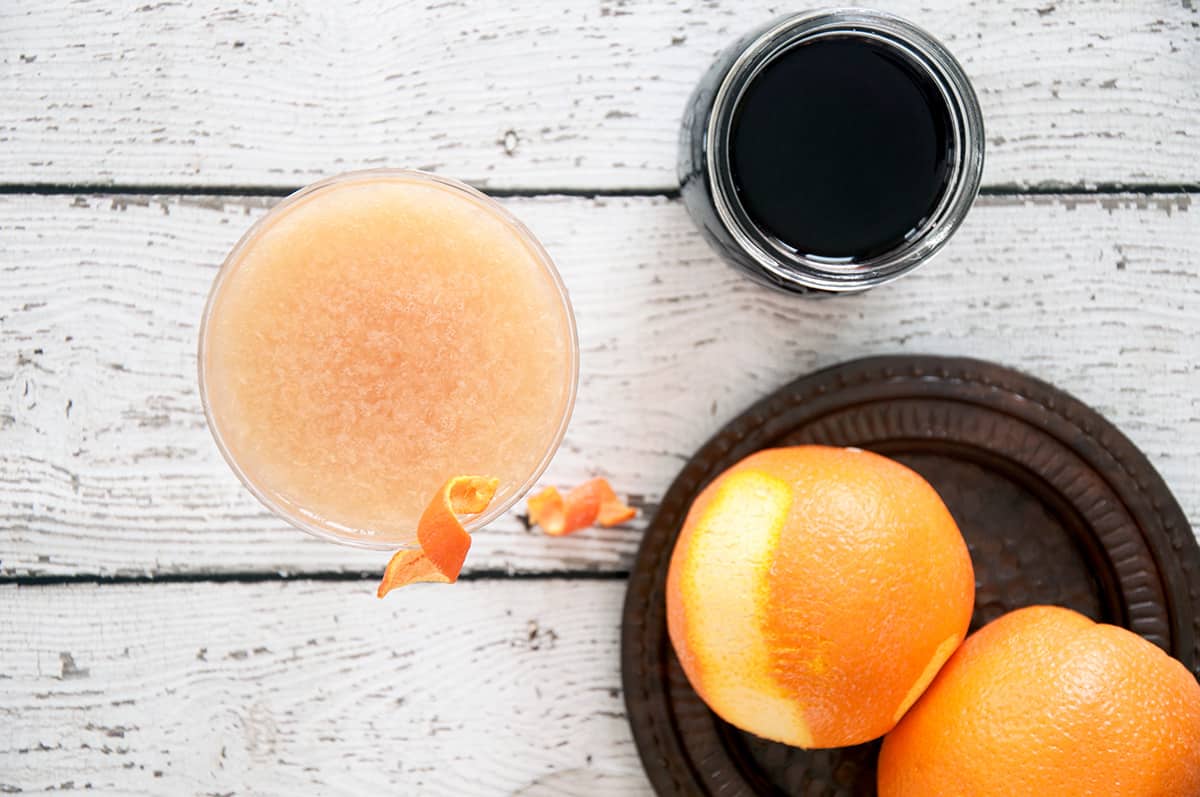 Overhead picture of a Monkey Gland cocktail with grenadine and an orange to the side.