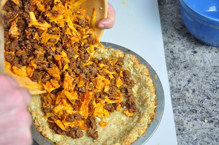 Pouring beef Dorito mixture into tater tot pie crust.