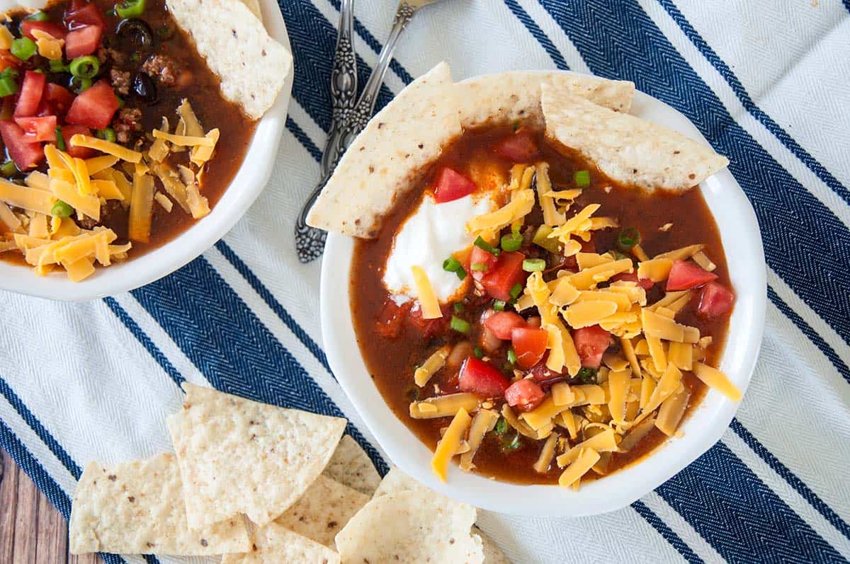 Two bowls of taco soup with cheddar cheese and sour cream on top.