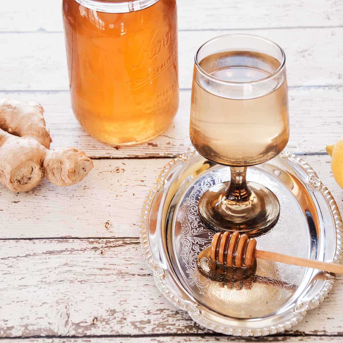 A glass of hot ginger tea with a bit of honey dipper covered with honey and ginger in the background.