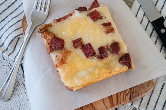 One Slice of Rueben Pizza on a parchment paper and cutting board