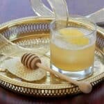 Gold Rush Cocktail on a Gold Platter with honey and a honey dipper to the side