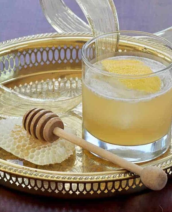 Gold Rush Cocktail on a Gold Platter with honey and a honey dipper to the side