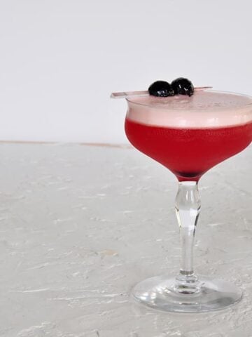 A Single Sam Ross Sour Cocktail on a white backtdrop and garnished with two maraschino cherries