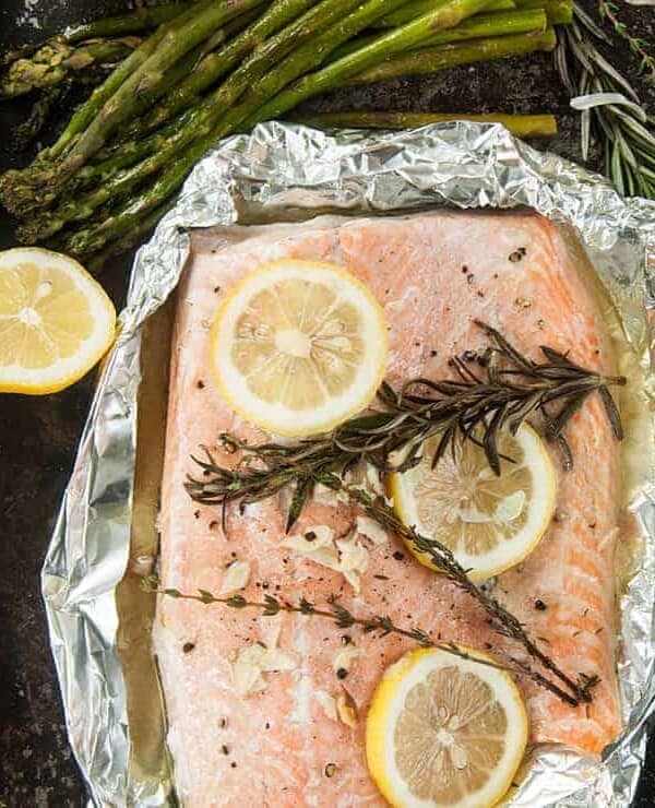 Overhead view of a tin foil grilled salmon fillet recipe, still in foil and some asparagus on the side.