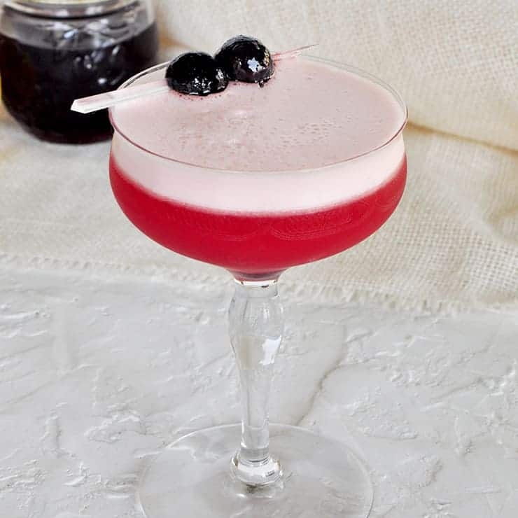 Overhead shot of a Sam Ross Sour Cocktail against a white backdrop with a bit of grenadine in a small mason jar. 