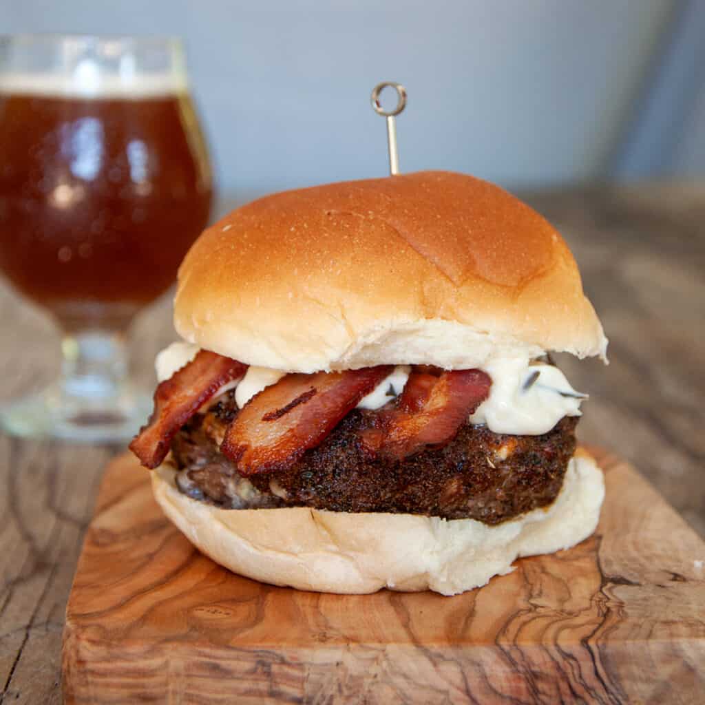 Black and Blue Burger on a cutting board with a pint of beer in the background.