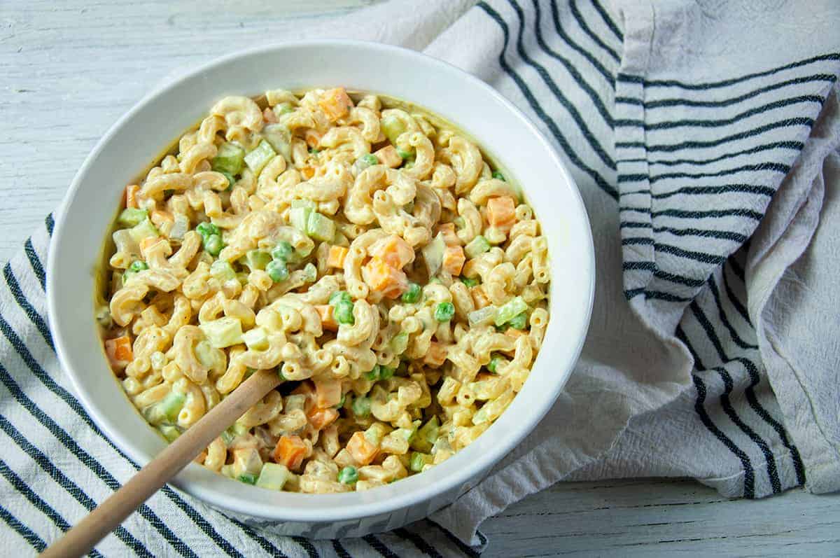 Rancharoni Macaroni in a dish, but on a white and blue towel with a wooden spoon in the bowl.