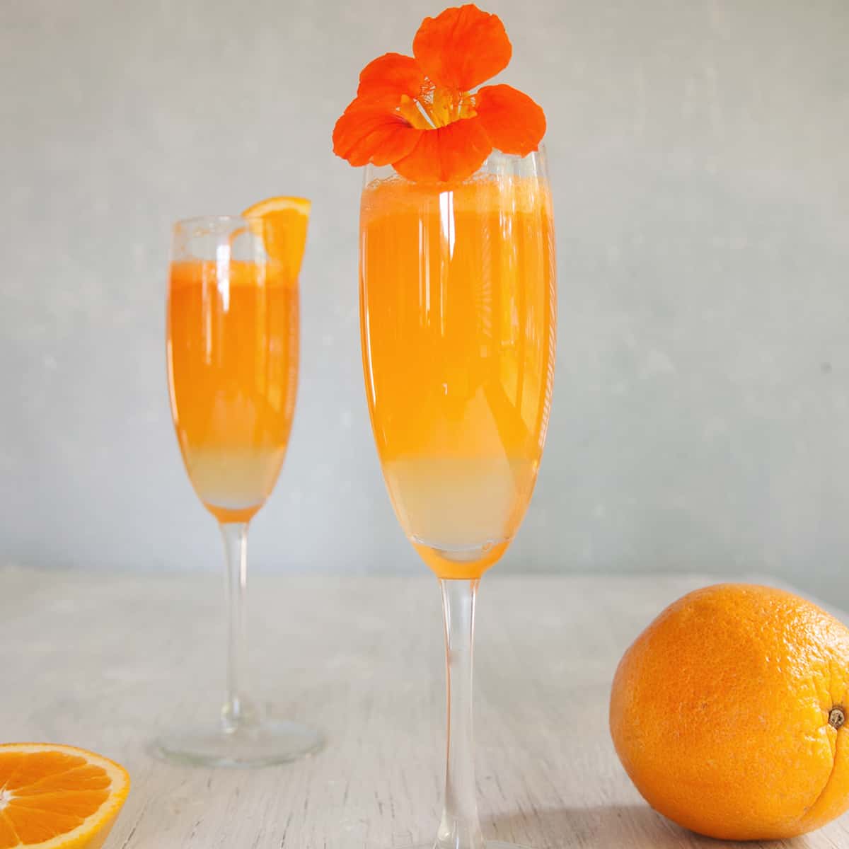 Two sprits prosecco cocktail s on a plain backdrop with a few oranges
