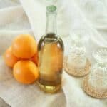 Liter bottle of Orangecello with 4 oranges and two glasses beside the bottle.