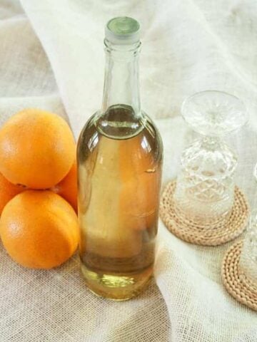 Liter bottle of Orangecello with 4 oranges and two glasses beside the bottle.