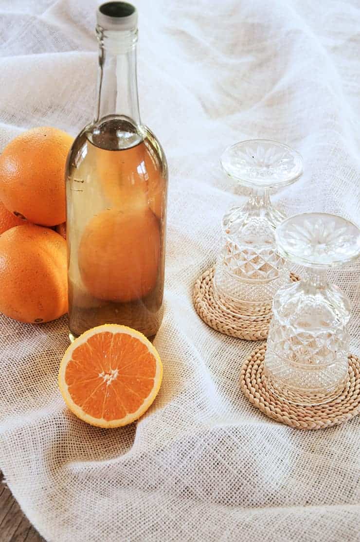 A bottle of orangecellow with a half orange showing in front of the bottle. Two glasses are showing.