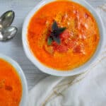 A bowl of Rustic Tomato Soup with some basil as a garnish on a white table