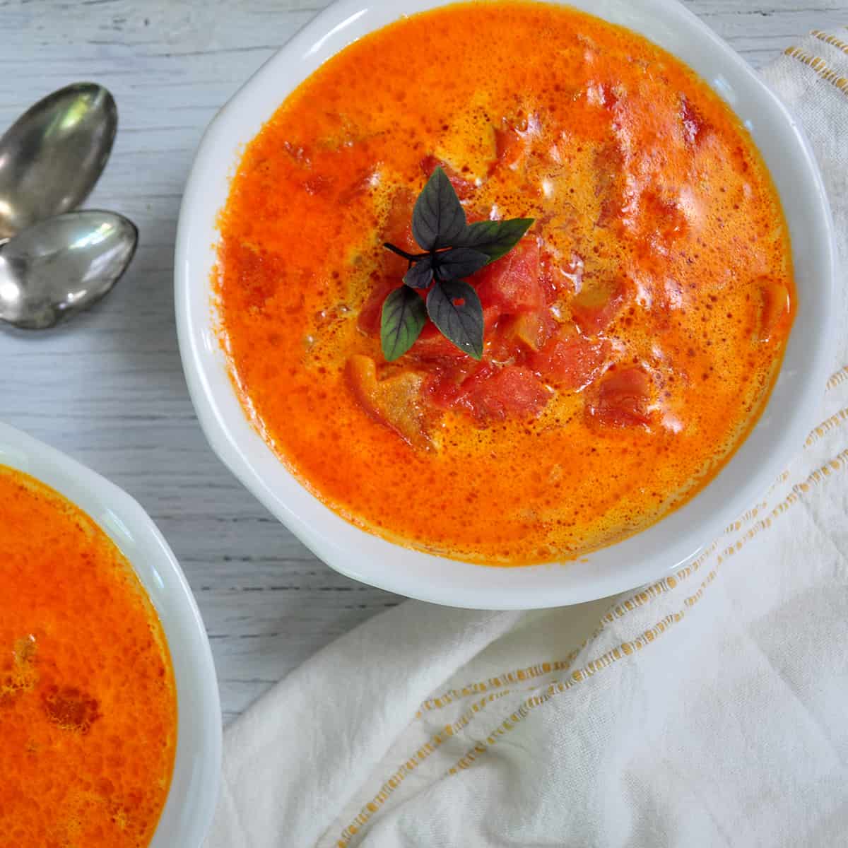 A bowl of Rustic Tomato Soup with some basil as a garnish on a white table