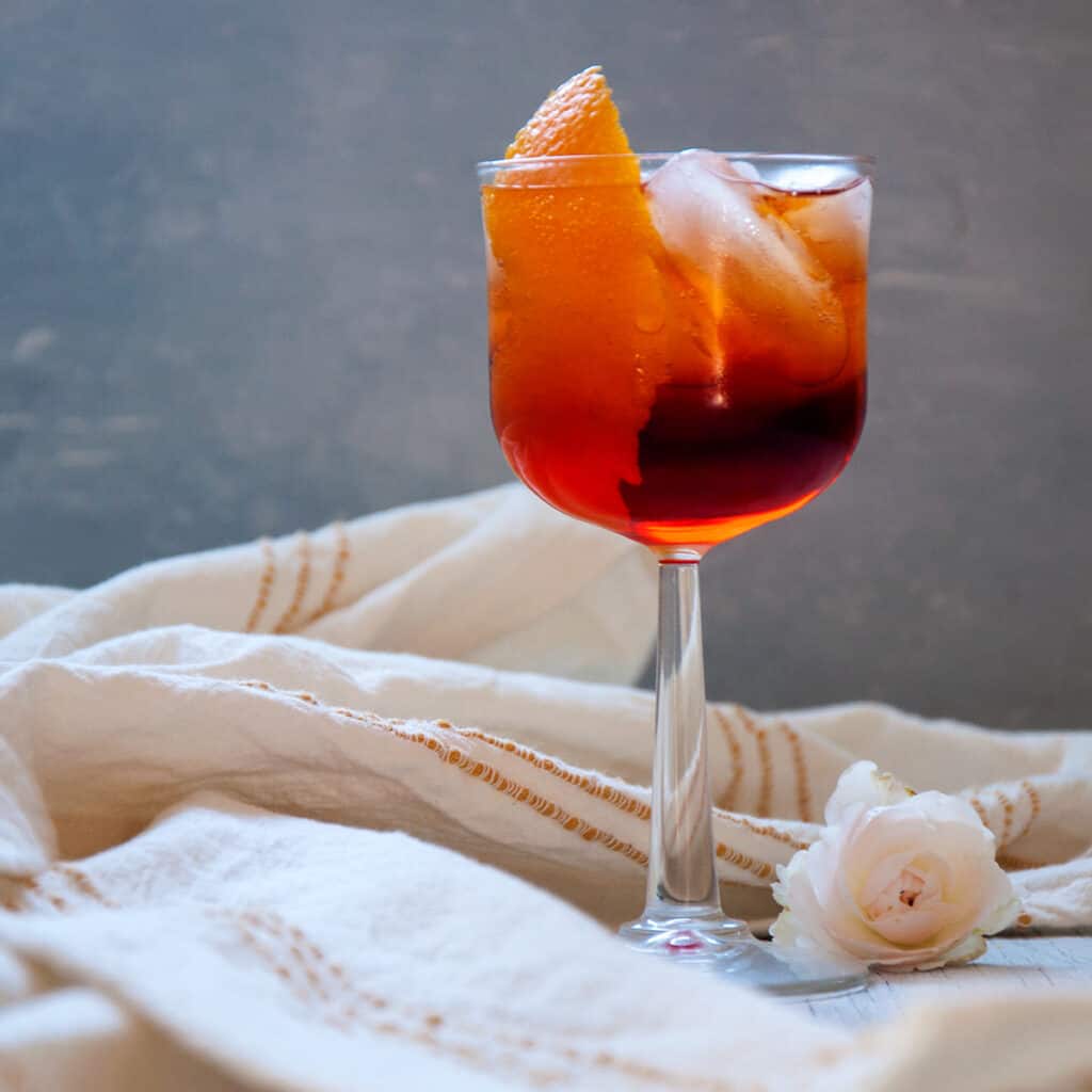 Aperol Americano Cocktail with a white napkin and flower on the table.