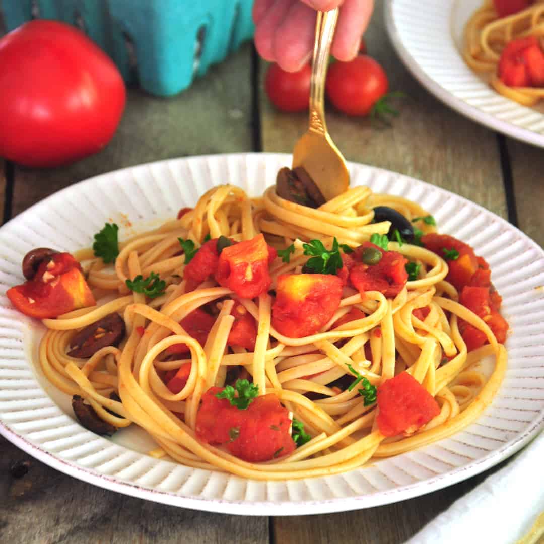 Twirling linguine and Puttanesca sauce around gold fork and getting ready to eat.