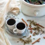 Two coffee mugs of this glogg recipe on a white sheet with spices in the background.