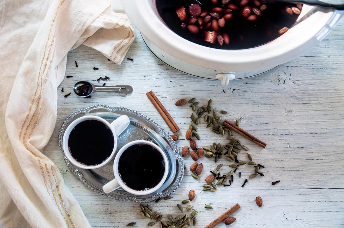 Two cups of glogg with a slow cooker full of the drink.