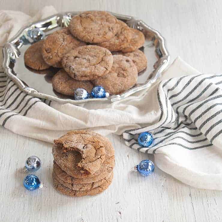 Stack of Ginger Cookies with one that has a bite taken out of it and a platter of extras in the background.