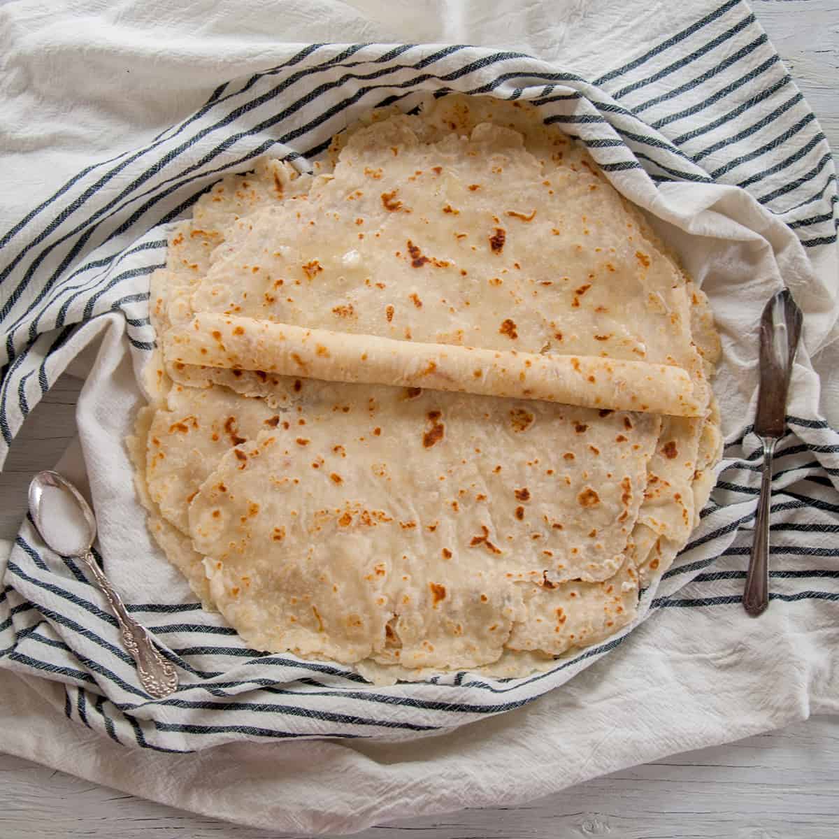 Flat lefse being rolled on a blue napkin. 