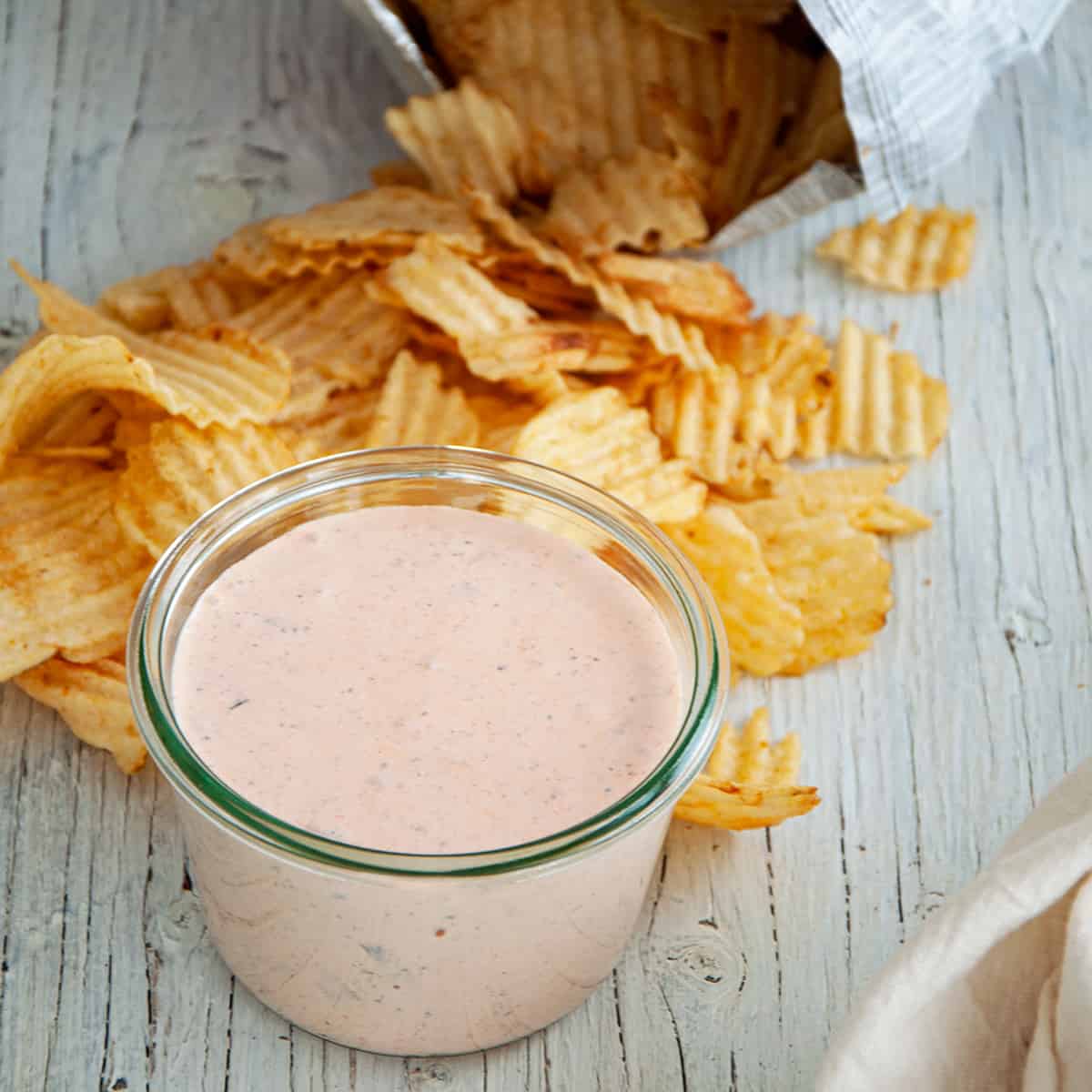 Mason jar filled with chip dip recipe on a white table with potato chips laying around it.