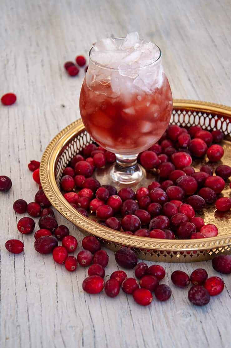 A glass of Purple Haze drink on a gold platter with cranberries all around.