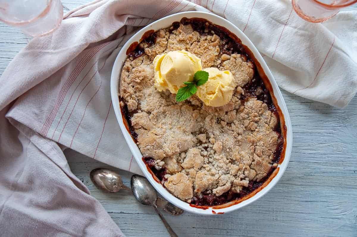 Overhead view of 1.5 Quart Baking dish full of cooked Strawberry Rhubarb Cobbler and two scoops of vanilla ice cream on top, garnished with mint.