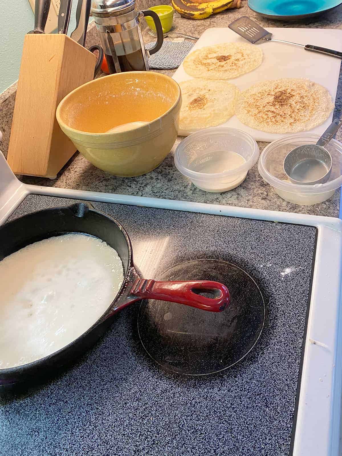 Testaroli frying in a cast iron pan and the batter setup off to the side.