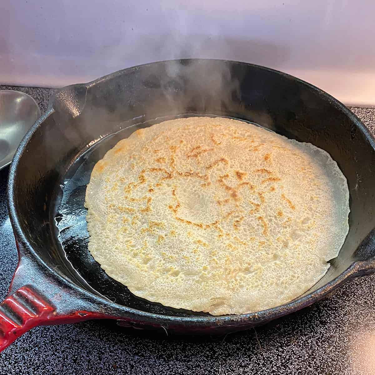 A single testaroli cooking in a cast iron, after having been flipped.