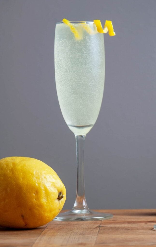 A single French 76 cocktail on a butcher block board and a lemon to the side.