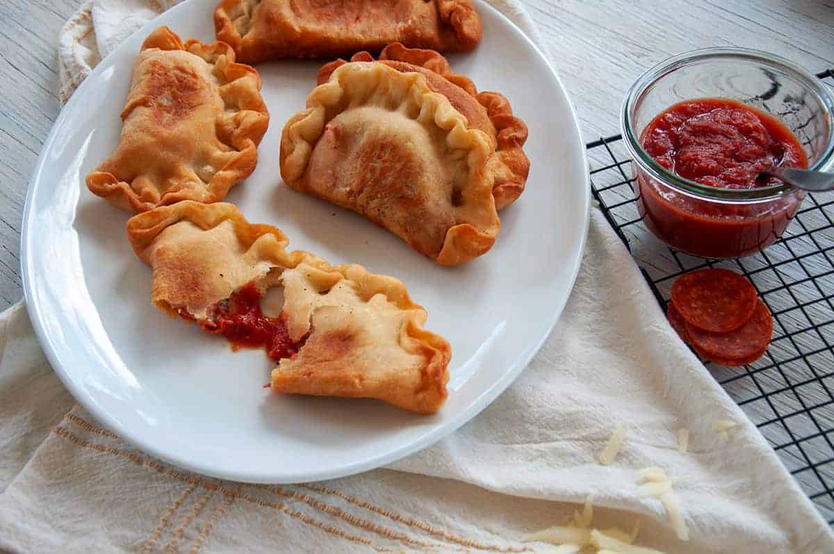 Four panzerotti on a big plate with one of them pulled apart to show the inside filling.