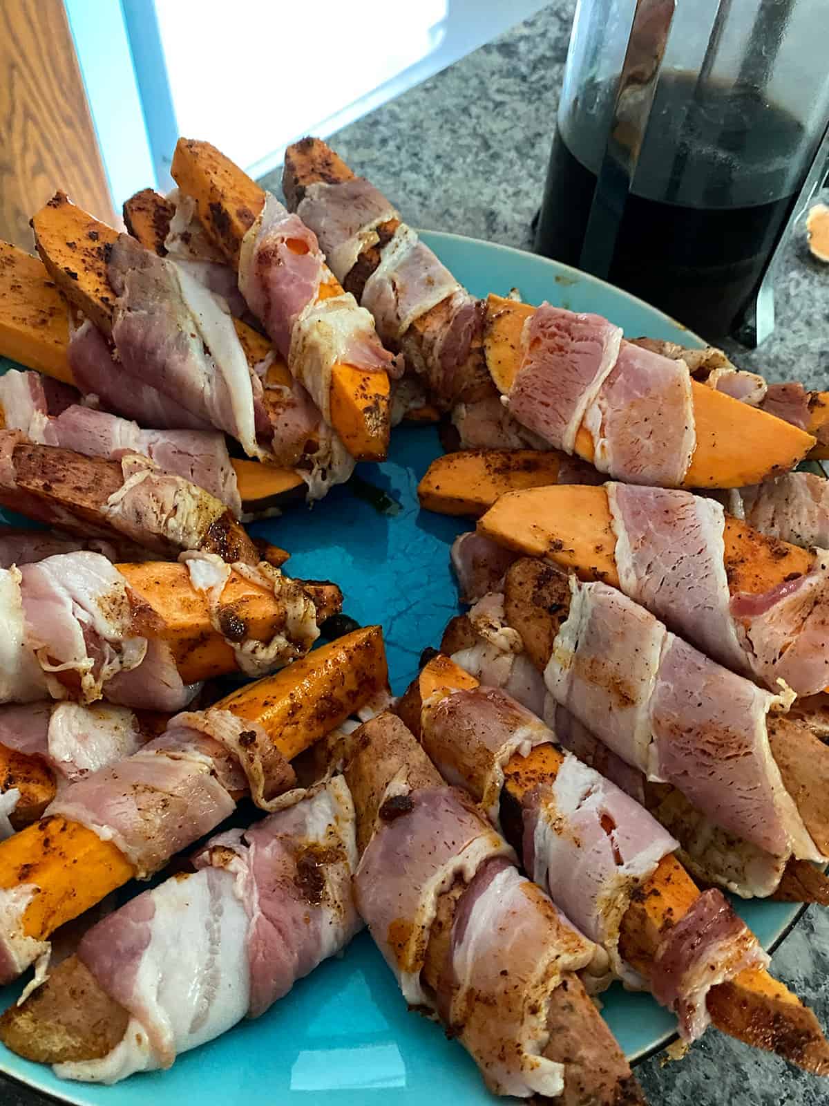 Process picture depicting sweet potatoes wrapped in bacon and almost ready for the grill.
