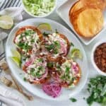 Four Honduran Enchiladas on top of a large white plate with red onions on the side, limes, and two gold forks.