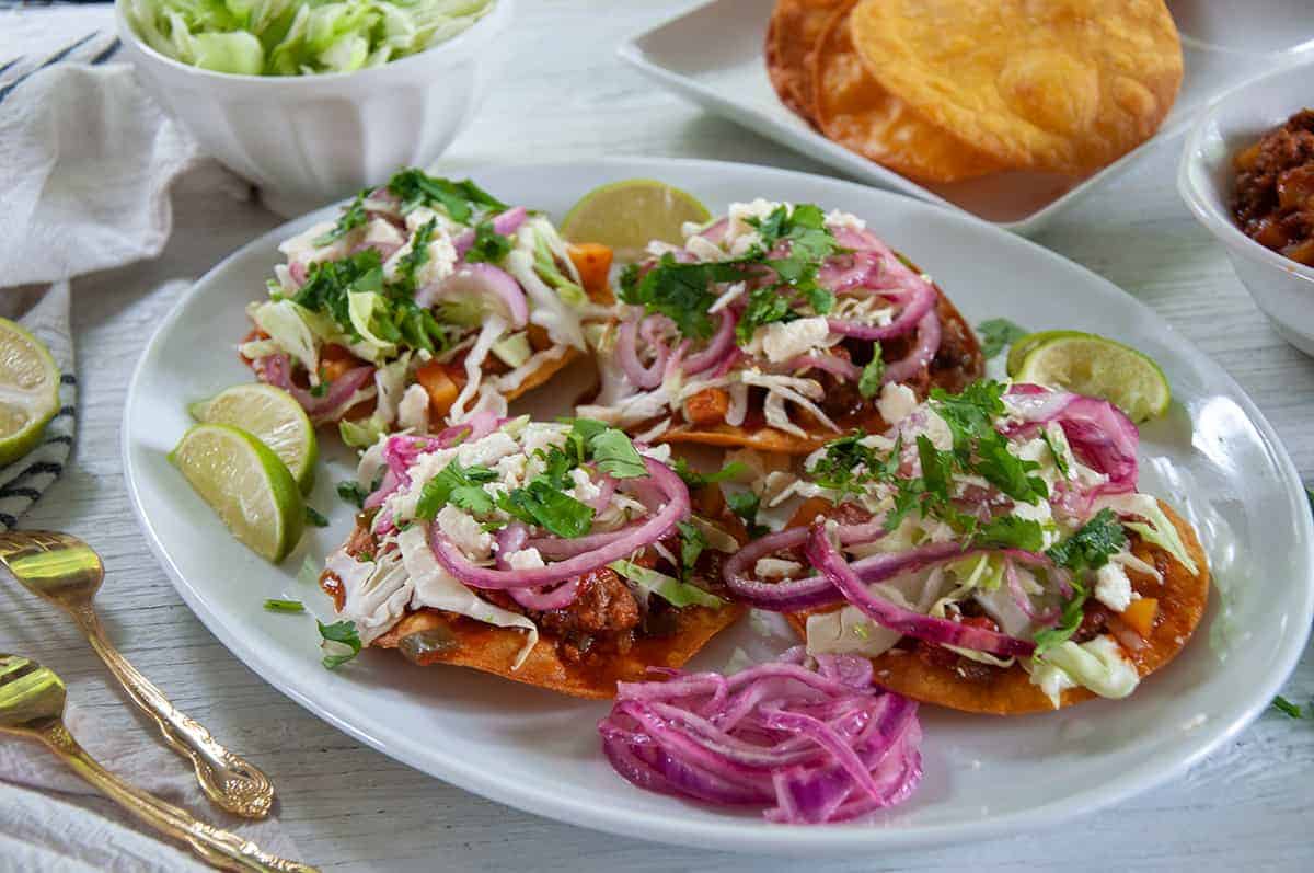 A big white platter full of Honduran Enchiladas, red pickled onions, and limes on the side.