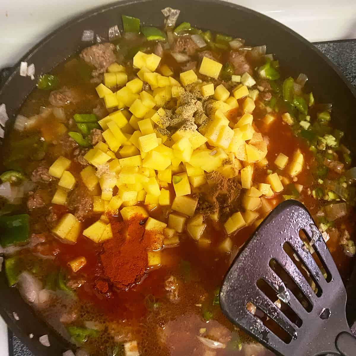 All filling ingredients added to a pan being brought to a simmering temperature and a spatula sitting on the side.