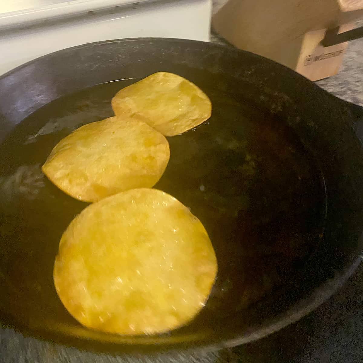 Three corn tortillas frying in hot oil in a cast iron pan.