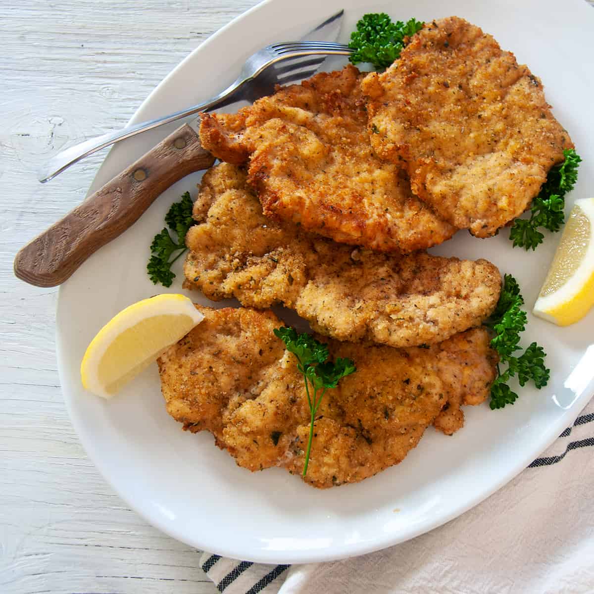 Four Pork Schnitzel cutlets on a large white platter, garnished with parsley and lemon.