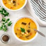 Two bowls of Caldo de Queso with oregano, pepper, and salt shown on the side.