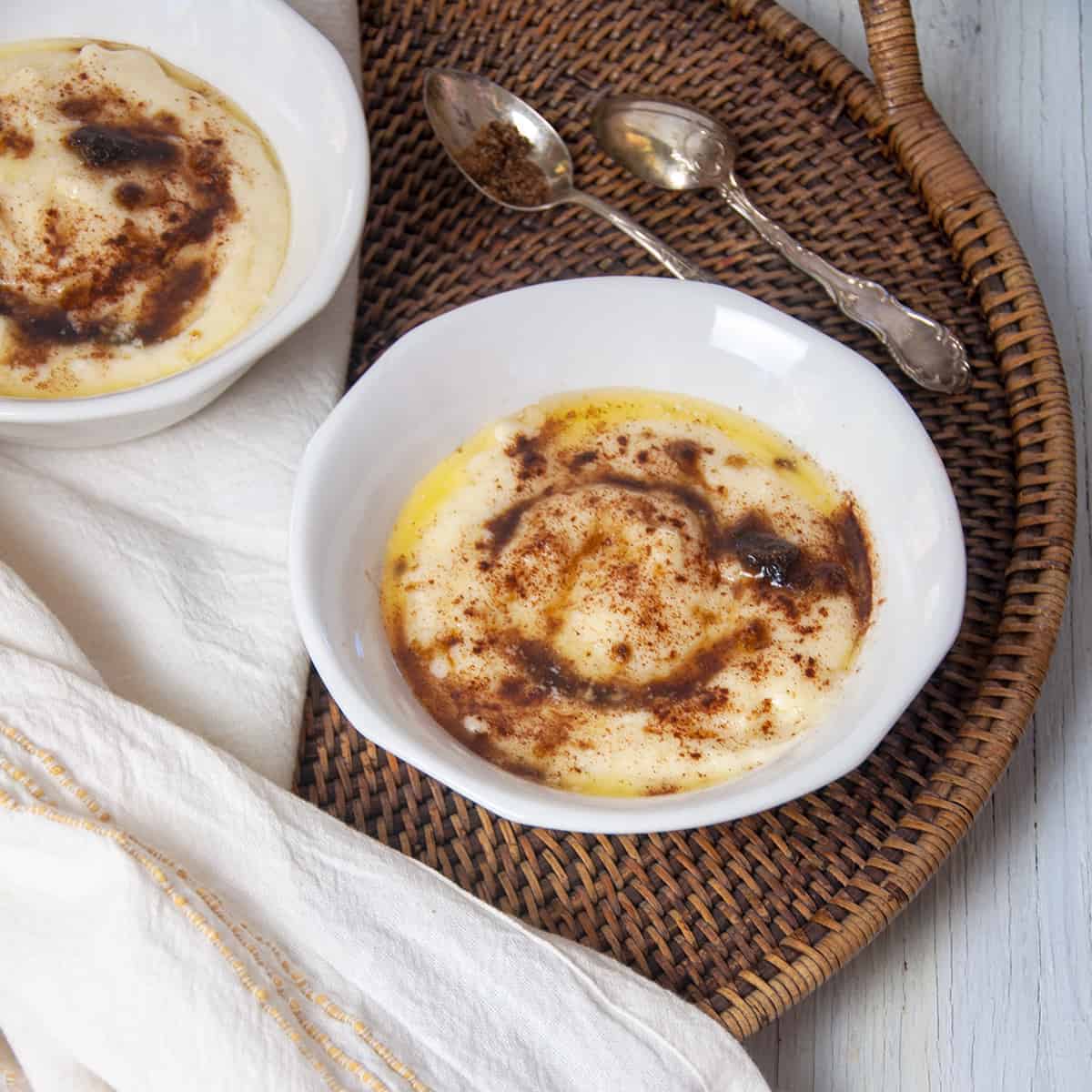 Rømmegrøt in a white bowl that is on a wicker platter with a white cloth to the side.