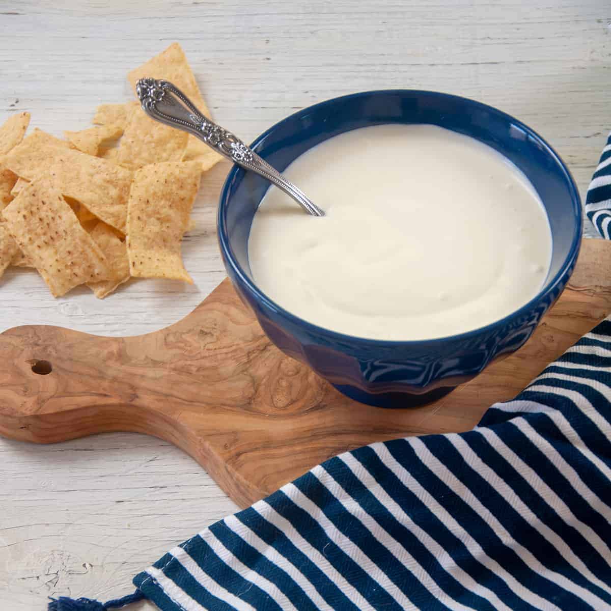 Bowl of homemade sour cream in a blue bowl that rests on a cutting board and chips.