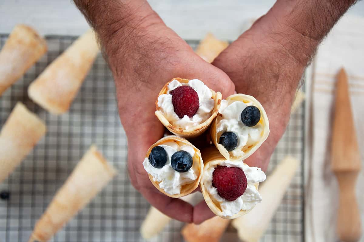 Holding four krumkakke in my hands over a cooling tray of unfilled krumkakke cones.