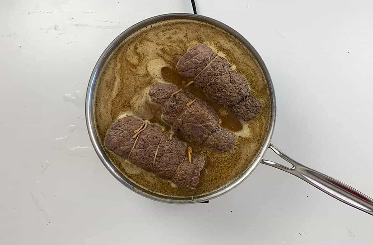 In large pan, three Rouladen are simmering in beef gravy.