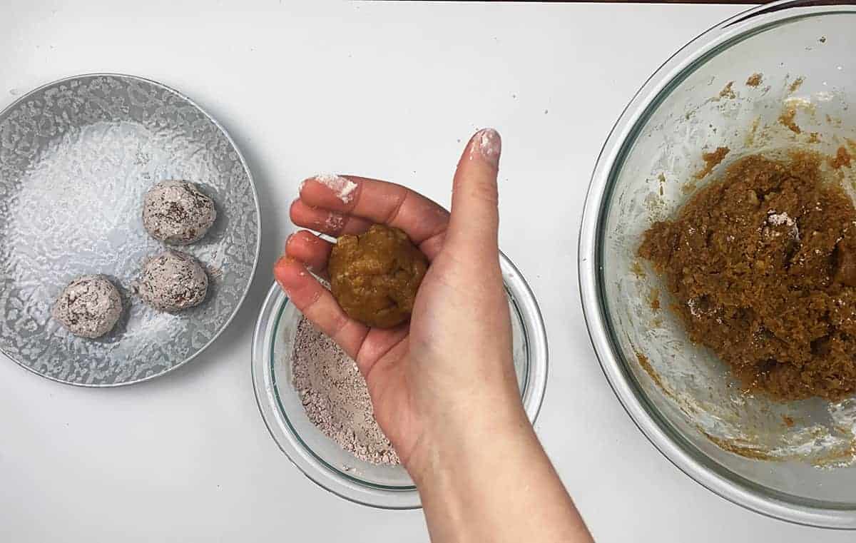 One rum ball being formed in a hand, but prior to be rolled in the outer coating, which is sitting right underneath the hand.
