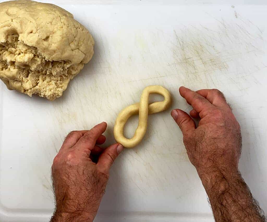 Forming a cookie into the infinity symbol on a white cutting sheet.